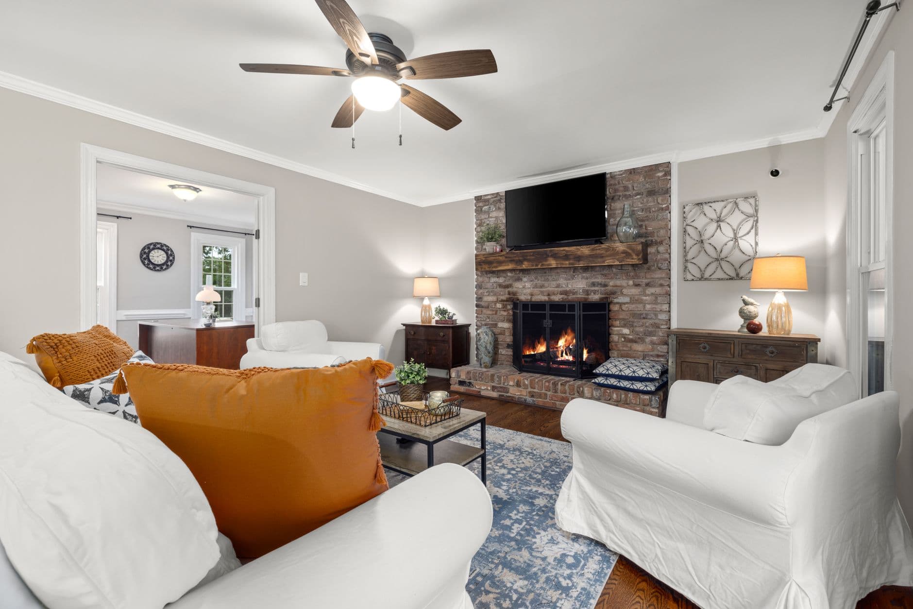 Inviting living room with a warm brick fireplace, orange accents, and classic decor.